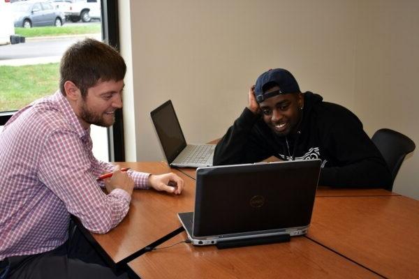 student and instructor sitting at a table with laptops laughing